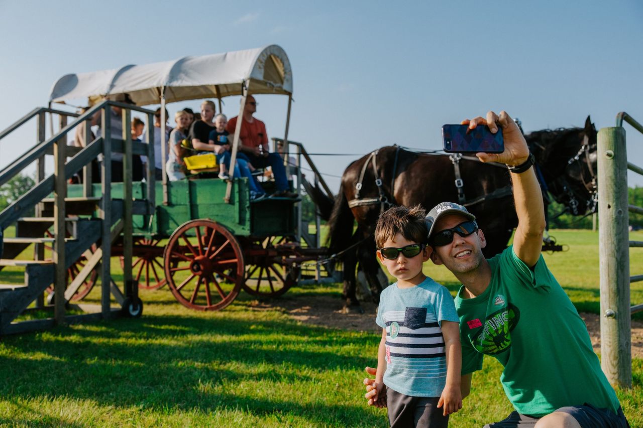 Man and child taking photo together in front of covered wagon.